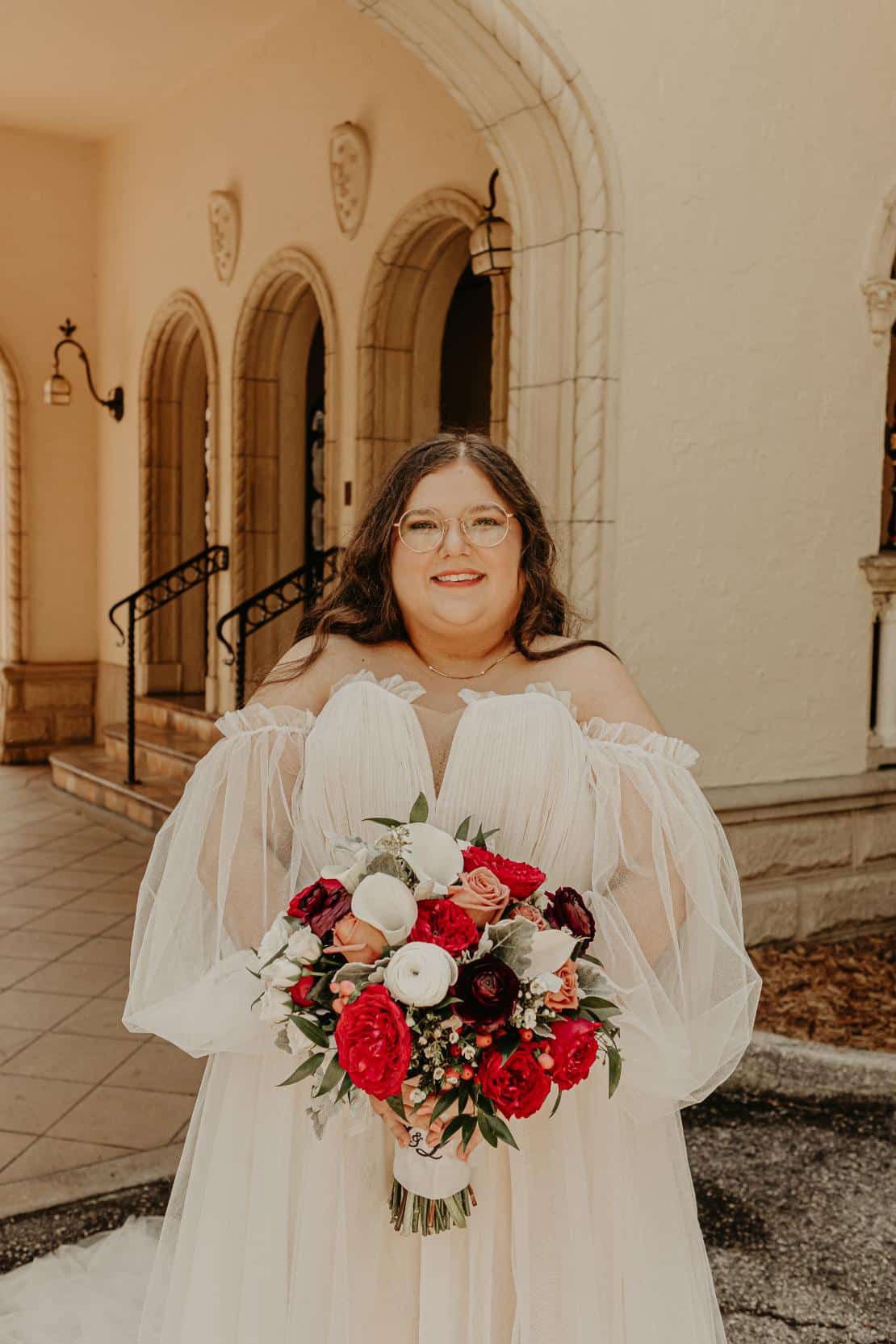plus-size wedding gown with sheer off-the-shoulder sleeves and a flowing tulle skirt, perfect for a timeless and elegant outdoor ceremony.