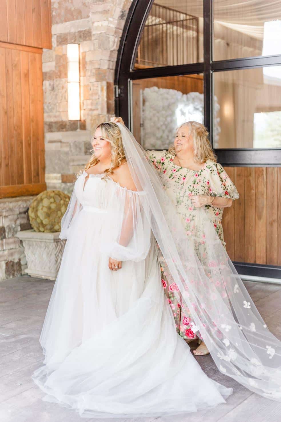 Romantic plus-size bridal gown featuring off-the-shoulder sheer sleeves, a flowing tulle skirt, and a dramatic cathedral-length veil, perfect for an ethereal and timeless wedding look.