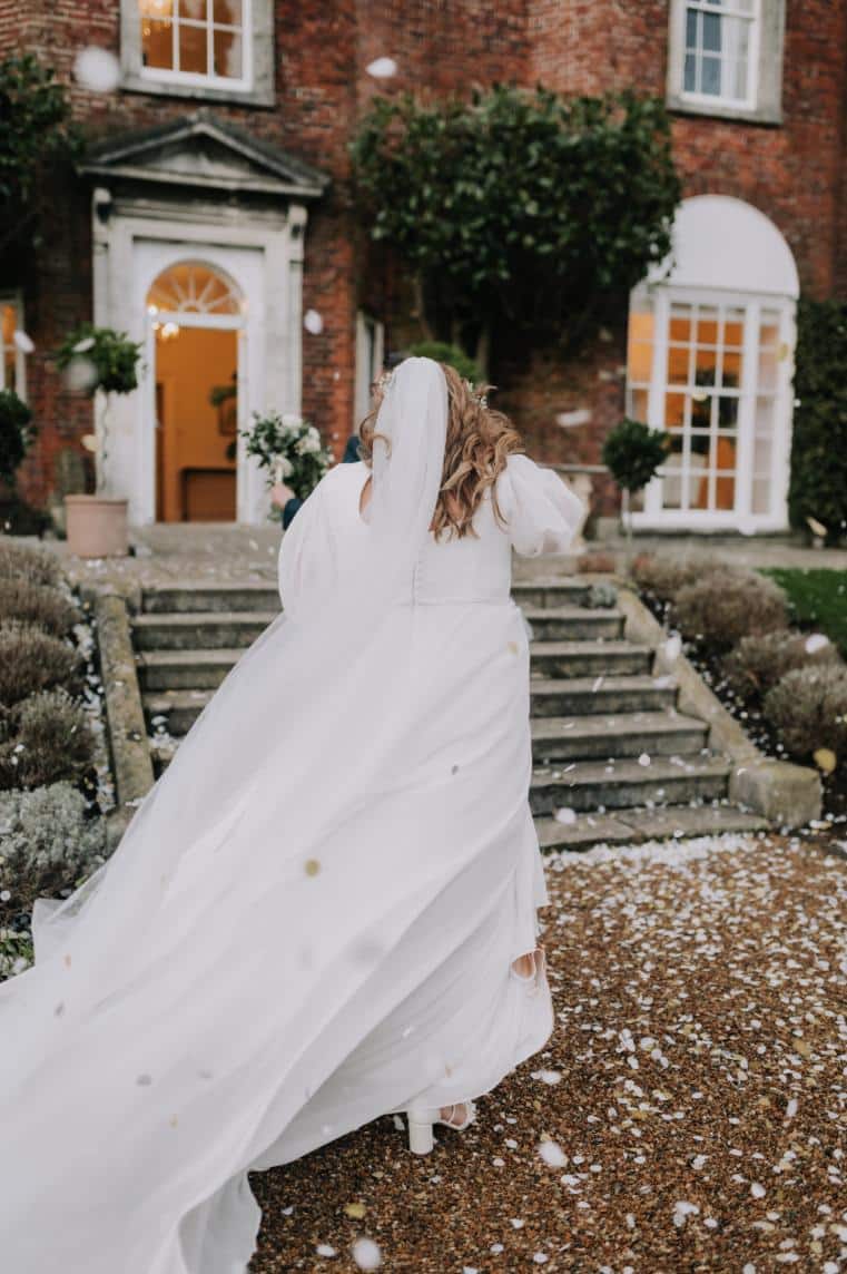 plus-size wedding gown featuring long sleeves, a plunging V-neckline, and a cinched waist with a jeweled belt, perfect for a timeless and sophisticated bridal look