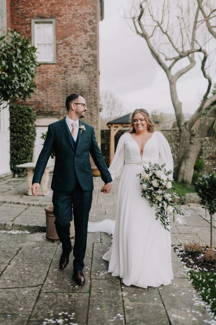 plus-size wedding gown featuring long sleeves, a plunging V-neckline, and a cinched waist with a jeweled belt, perfect for a timeless and sophisticated bridal look