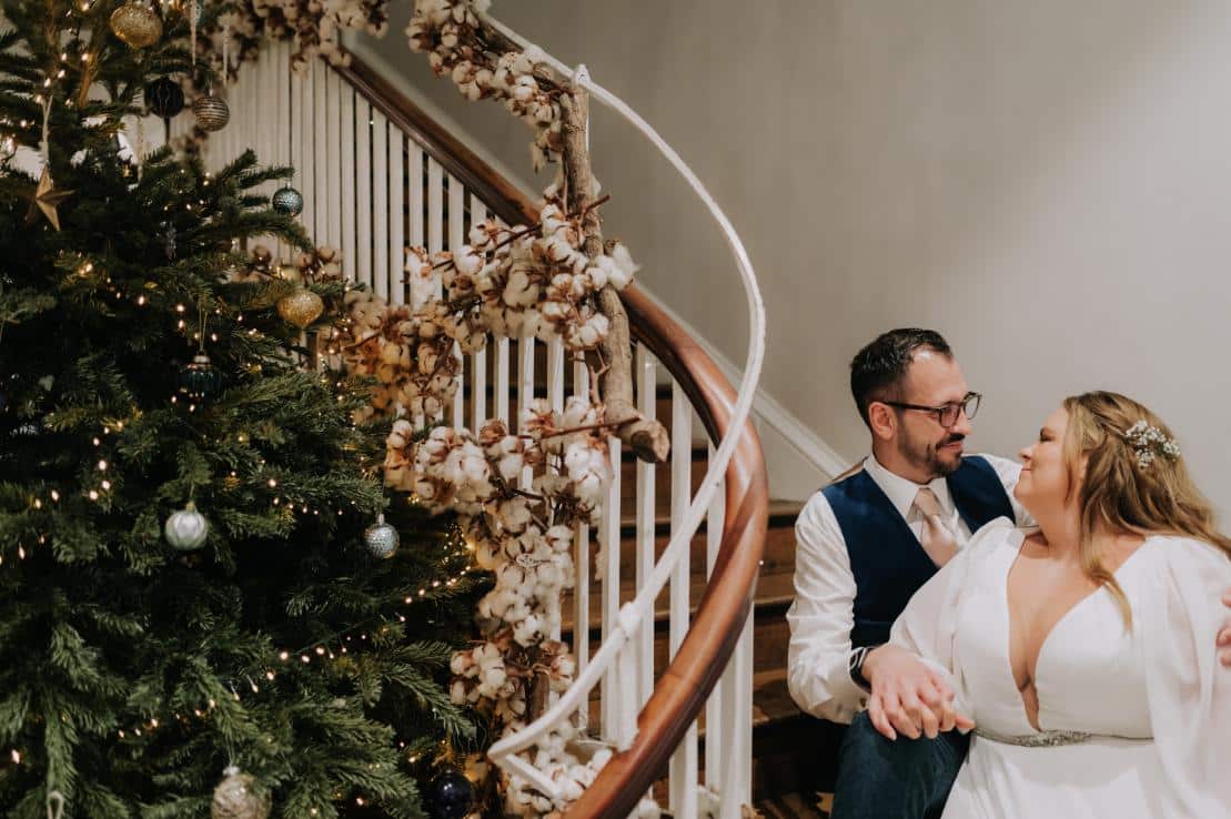 plus-size wedding gown featuring long sleeves, a plunging V-neckline, and a cinched waist with a jeweled belt, perfect for a timeless and sophisticated bridal look