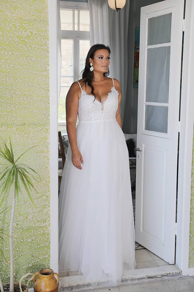 This plus-size bride looks stunning in an ethereal tulle A-line wedding dress. The gown features delicate spaghetti straps and a deep V-neckline adorned with intricate lace, creating a captivating bodice that is both feminine and elegant. The flowing tulle skirt adds a dreamy quality, perfect for a romantic garden or outdoor wedding, while the overall look remains effortlessly sophisticated and timeless.