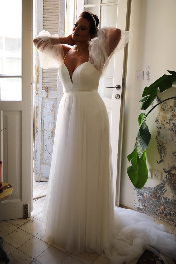Elegant plus-size bride glowing in a romantic gown with ethereal tulle puff sleeves and a plunging neckline. The airy, flowing skirt enhances her graceful silhouette