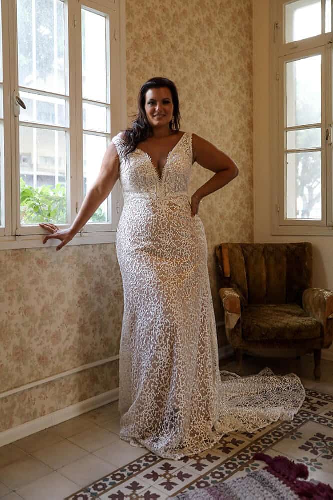 Gorgeous plus-size bride in a stunning lace wedding gown featuring a deep V-neckline and fitted silhouette. The intricate lace pattern gracefully accentuates curves, exuding confidence and timeless elegance for a captivating bridal look.