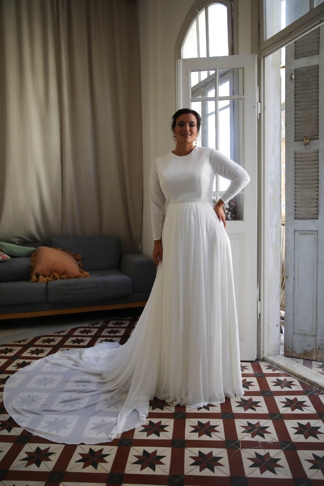 The plus-size bride, dressed in a simple yet elegant long-sleeve gown with a flowing skirt and train