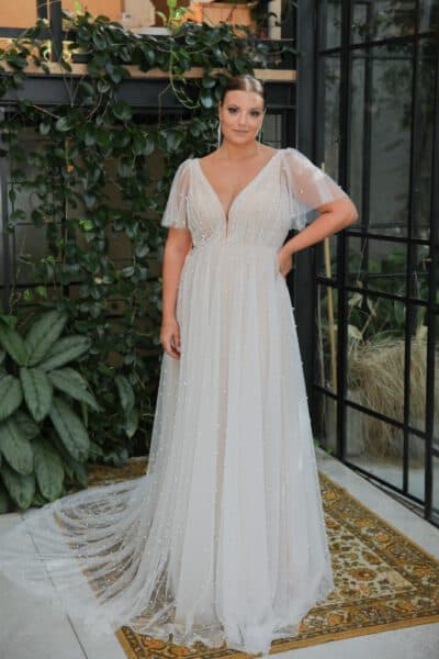 Plus-size bride in a delicate pearl-adorned tulle wedding gown with flutter sleeves and a deep V-neckline