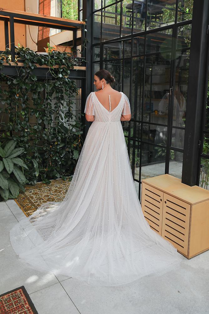 The plus-size bride, wearing a flowing gown with sheer sleeves and intricate beadwork