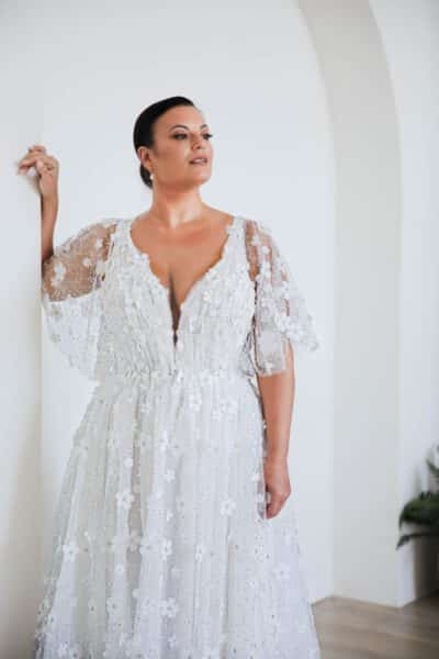 Plus-size bride in a floral lace wedding gown with flutter sleeves and a plunging neckline