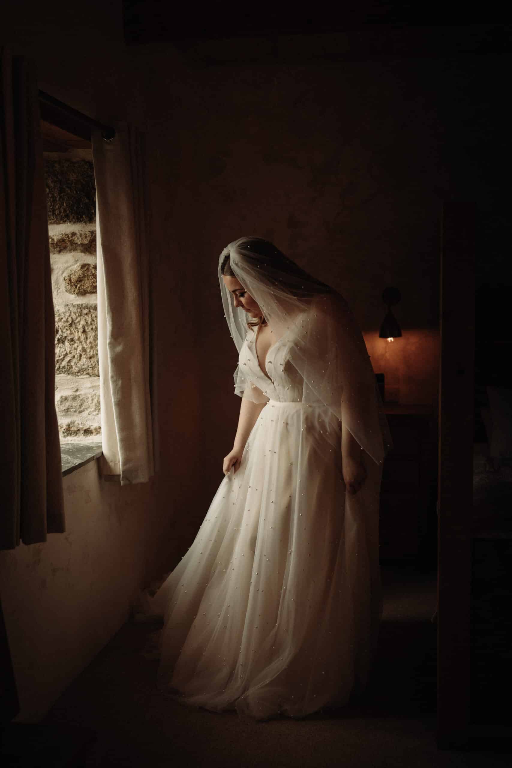 The bride, in a pearl-embellished dress and veil, holds a dimly lit room.