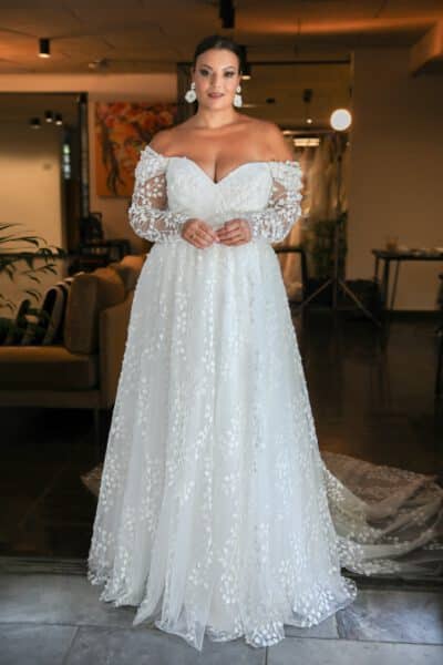 Plus-size bride in an off-the-shoulder lace wedding gown with long sleeves and floral appliqués