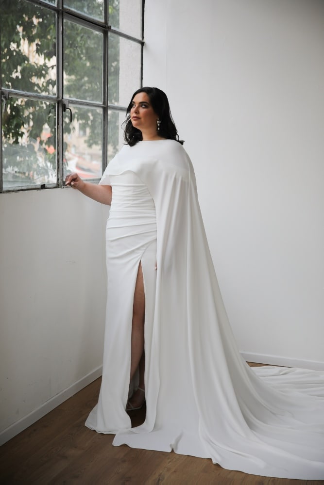 Plus-size bride in a sleek off-the-shoulder wedding gown with a sweetheart neckline and a long train and a cape