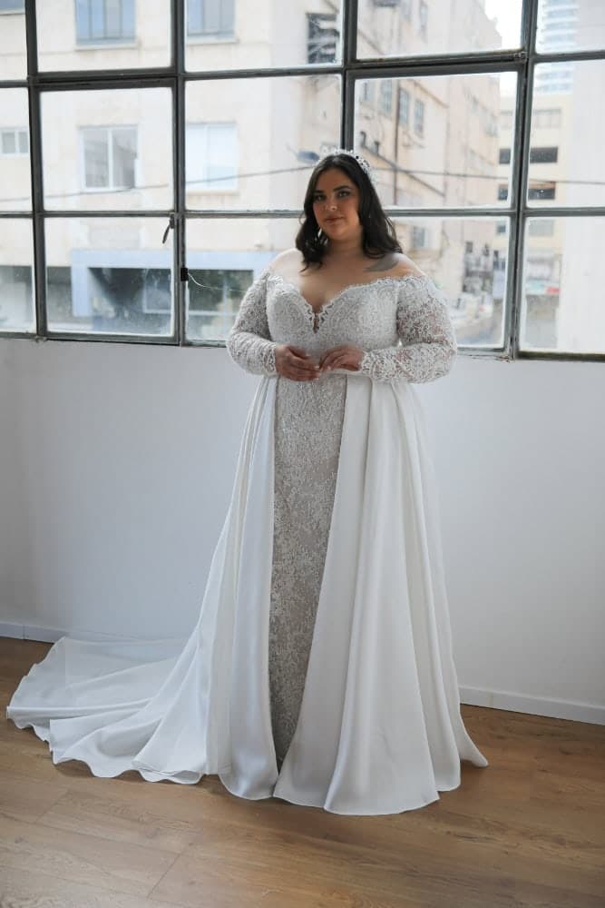 Plus-size bride in a lace wedding gown with long sleeves, a deep sweetheart neckline, and an overskirt
