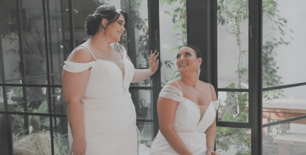 Two brides smiling at each other indoors