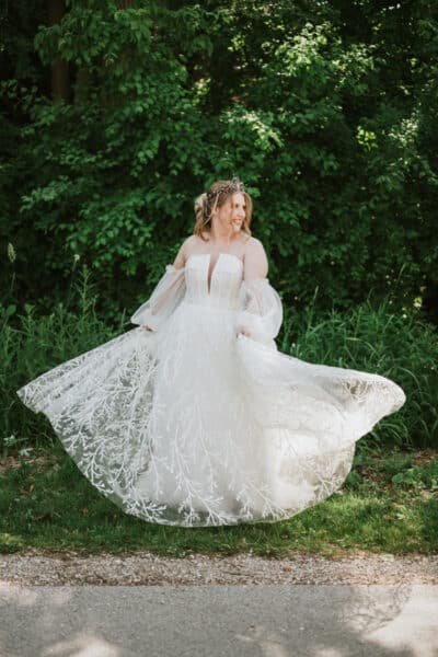 "Plus-size bride twirls in her customized wedding gown featuring ethereal bishop sleeves, intricate botanical lace, and a dramatic neckline, radiating elegance and individuality."