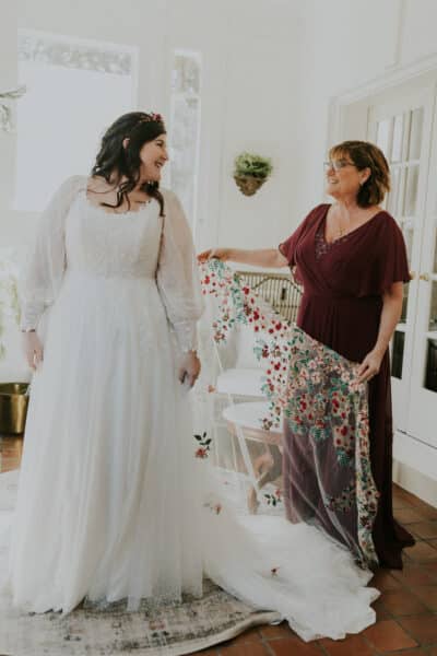 Plus-size bride beams in her customized sparkly gown with unique bishop sleeves, paired with a vibrant floral-embroidered veil, showcasing personal touches.