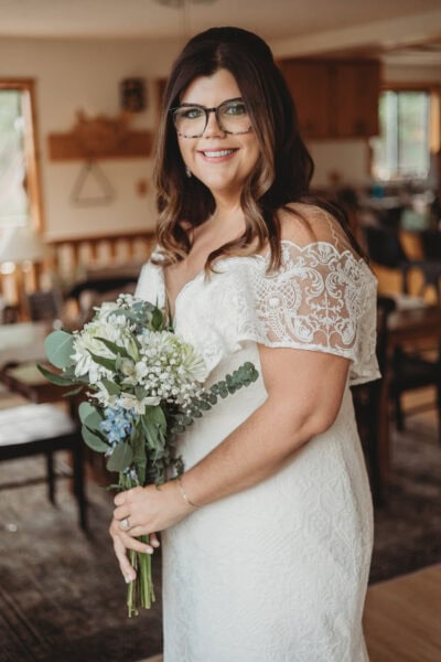 Meghan in the Sean gown by Studio Levana, a stunning plus-size boho wedding dress with an elegant off-shoulder design and lace train, holding a bouquet.